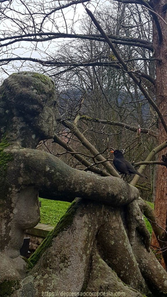 Um pássaro olha uma estátua entre as árvores secas do inverno. Representa a solidão. 